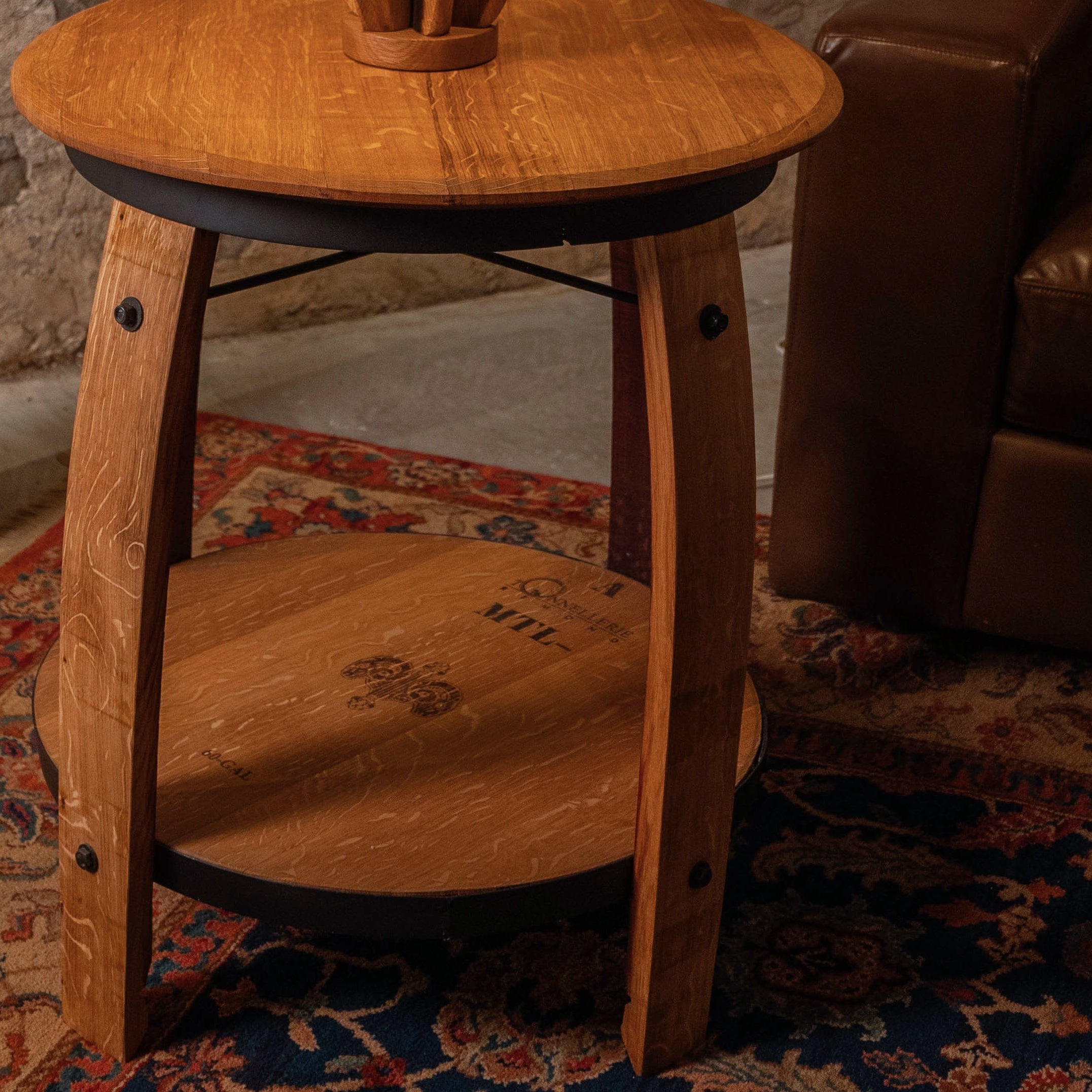 Close-up of the Casq Wine Barrel End Table showing the reclaimed barrelhead surfaces, oak stave legs, and cooperage markings on the lower shelf.