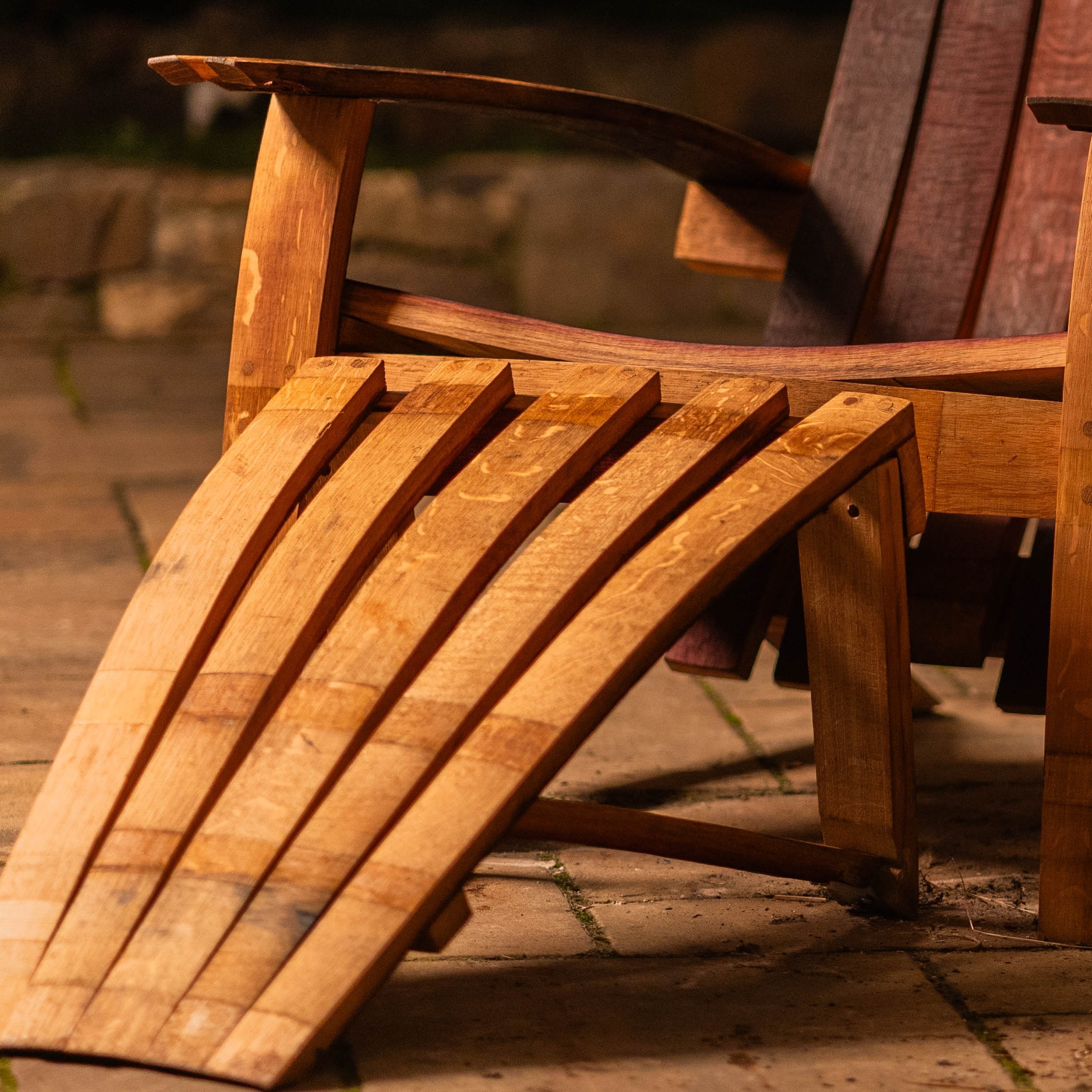 Close-up of the Cellr wooden Adirondack footstool paired with the matching Adirondack chair, showing the curved reclaimed wine-barrel staves and warm oak finish.