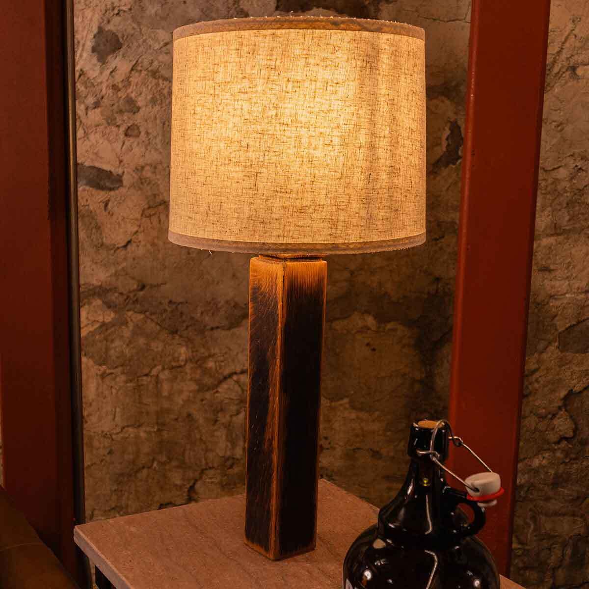 Charr Wooden Table Lamp with a fabric shade on a reclaimed barrel stave base, shown on a console table against a stone wall.