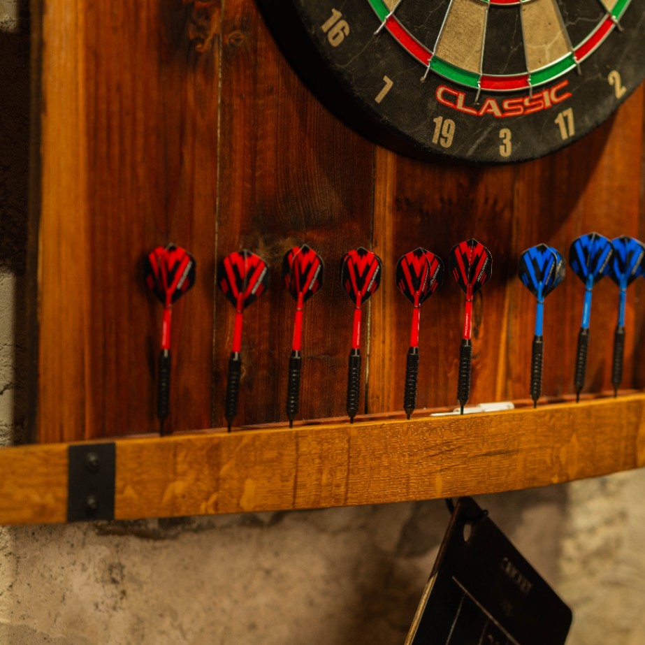 Close-up of red and blue darts stored in the wooden holder beneath the dartboard.