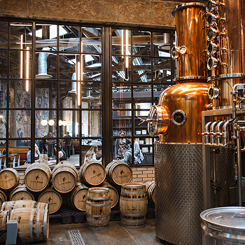 Industrial copper distillery surrounded by aging barrels, showing one source behind our reclaimed wood furniture.
