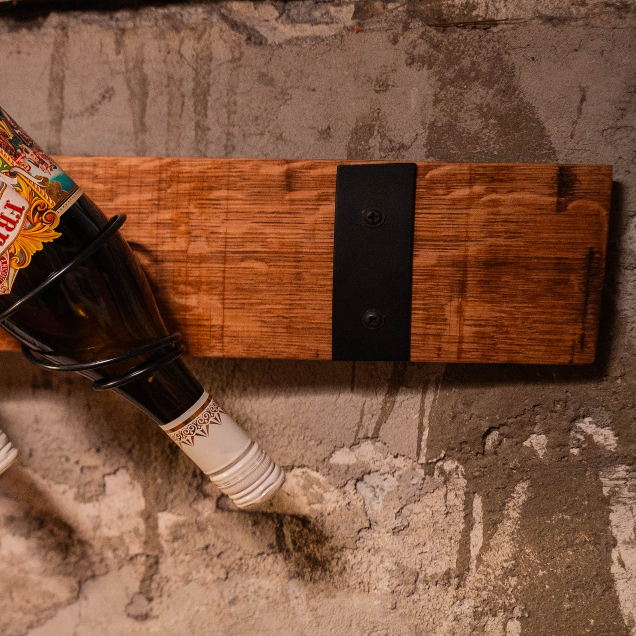 Close-up of a reclaimed barrel-stave wine rack showing a single bottle angled downward in the wall mount.