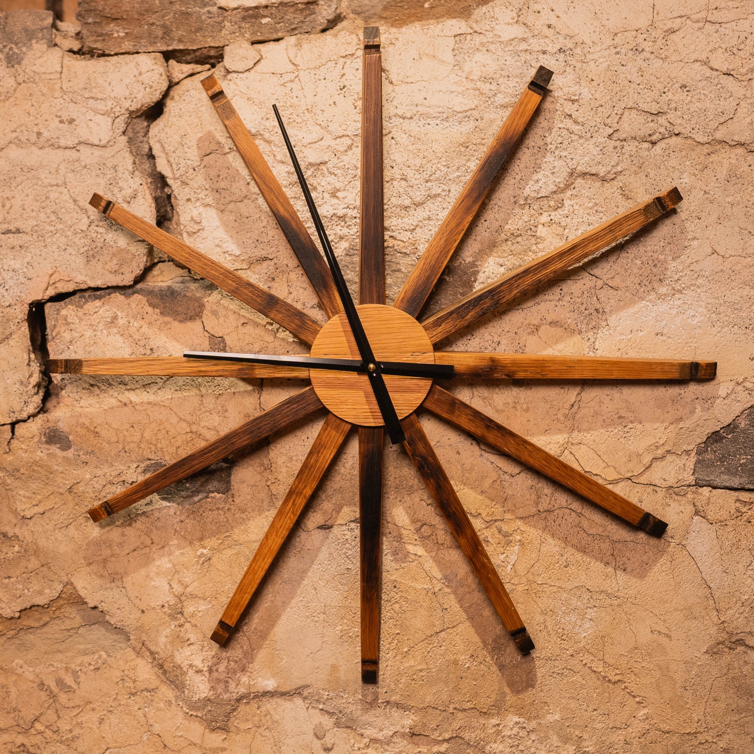 Large 24-inch wall clock handmade from reclaimed bourbon barrel staves, mounted on a textured stone wall.