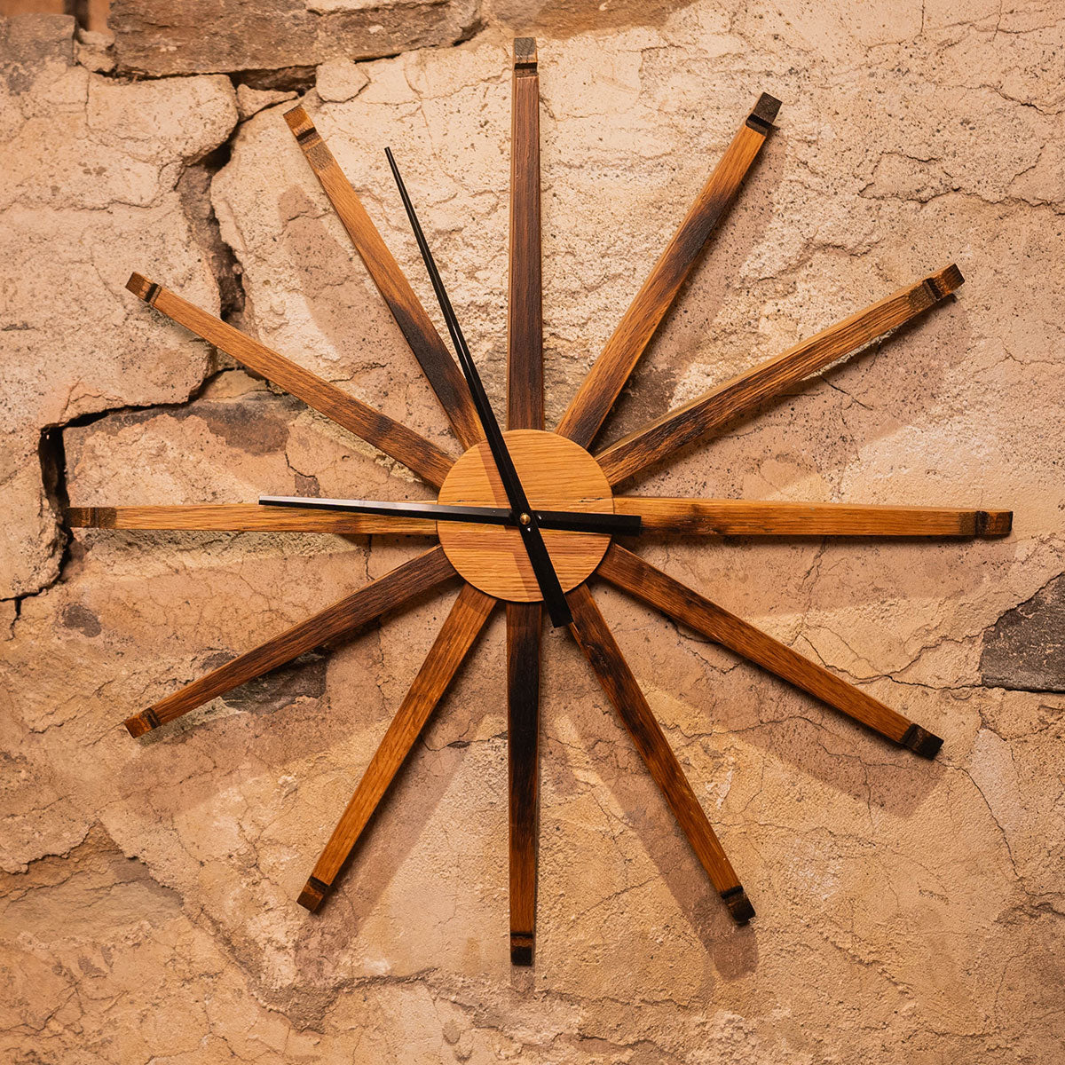 Large 24-inch wall clock handmade from reclaimed bourbon barrel staves, mounted on a textured stone wall.