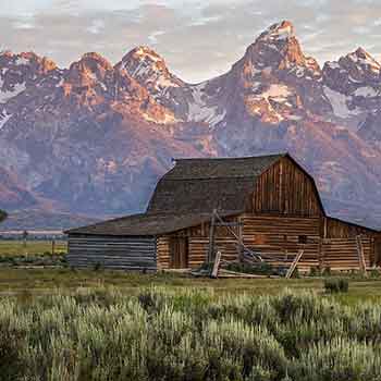 Old barn beneath mountain peaks, showing the inspiration behind rustic lighting & rustic home decor.