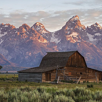 Old barn beneath mountain peaks, showing the inspiration behind rustic lighting & rustic home decor.