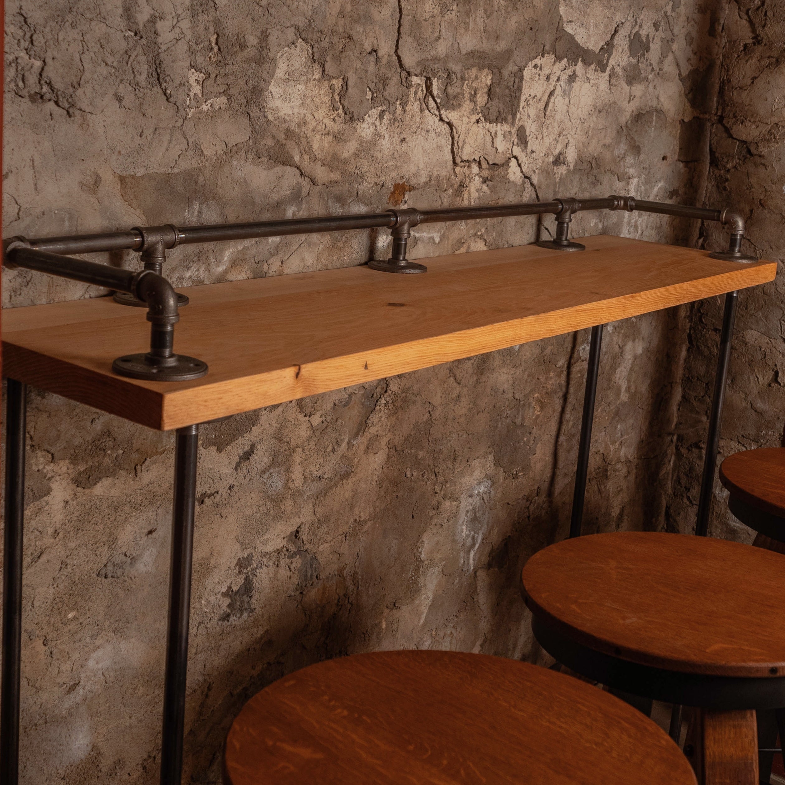 Side angle of the Planq High Top Bar Table displaying the reclaimed wood top, rear bar rail, and bar-height stools beneath.
