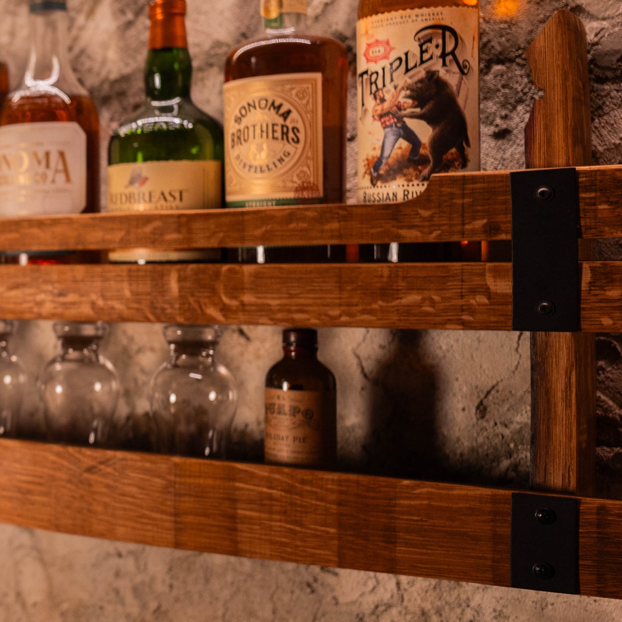 Close-up of wooden wall shelf with liquor bottles on the upper tier and glasses placed on the lower tier.