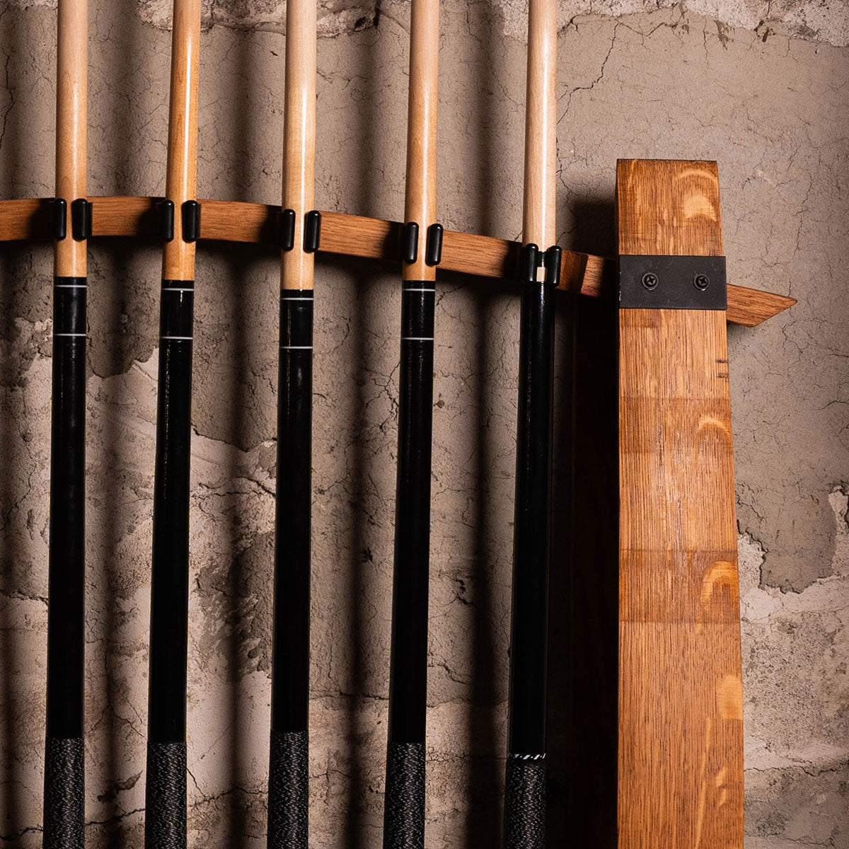 Close-up of pool cues snapped into quick-release clips on reclaimed barrel stave rack