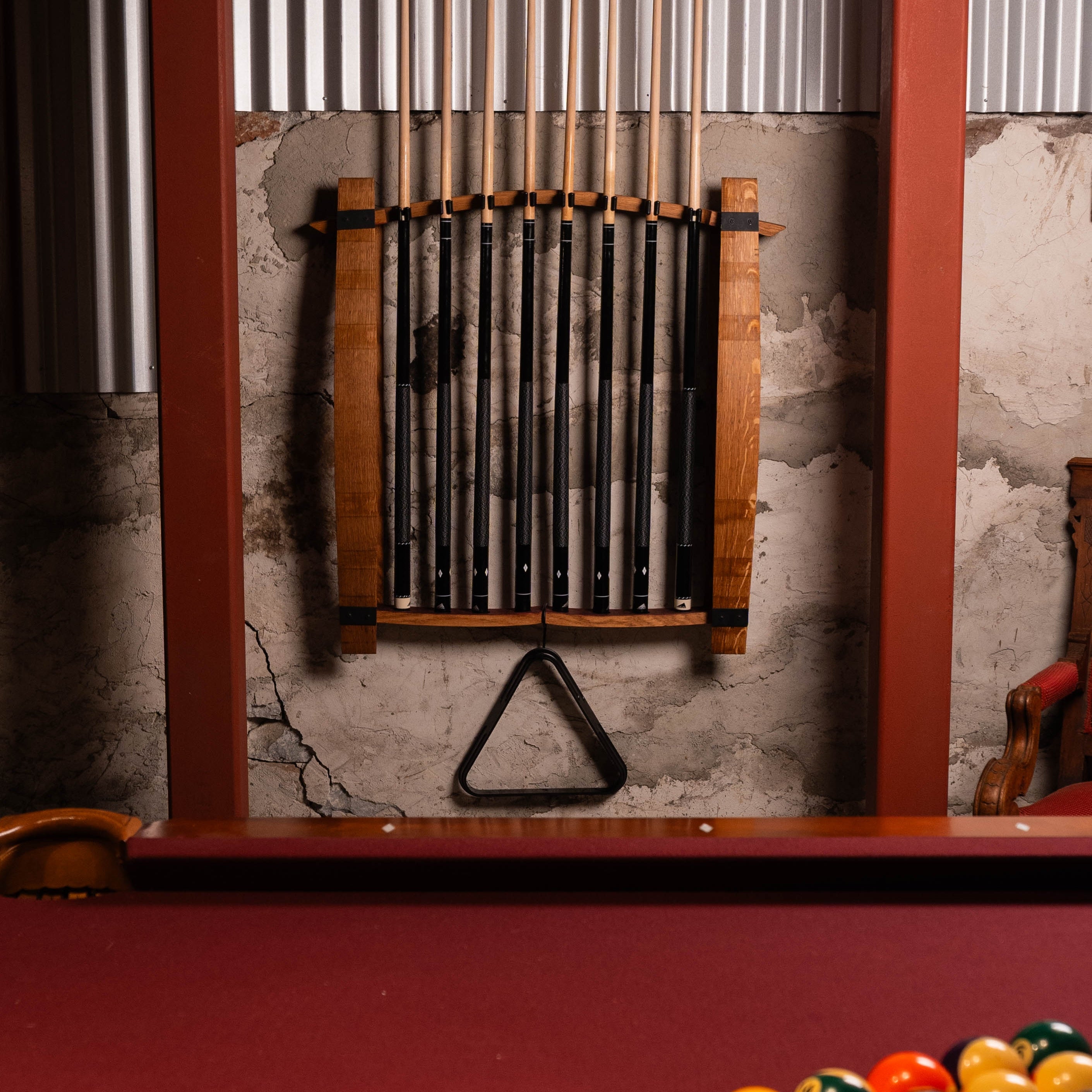 Wide shot of wall-mounted pool cue rack holding eight cues above a pool table