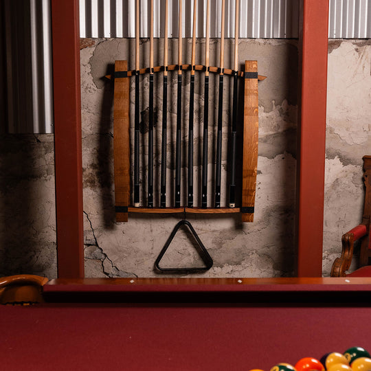 Wide shot of wall-mounted pool cue rack holding eight cues above a pool table