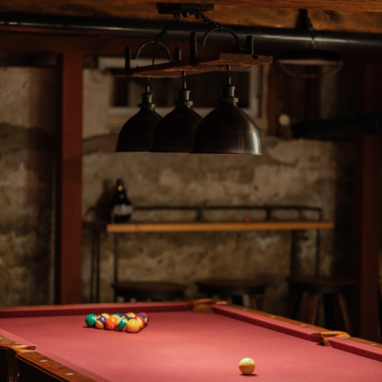 Pool table light fixture over a red velvet pool table in a rustic game room setting.