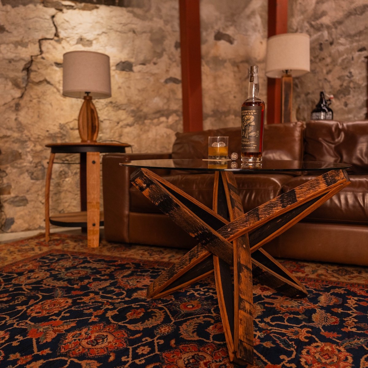 Home bar scene with leather sofa, whiskey barrel stave coffee table, and stone wall.