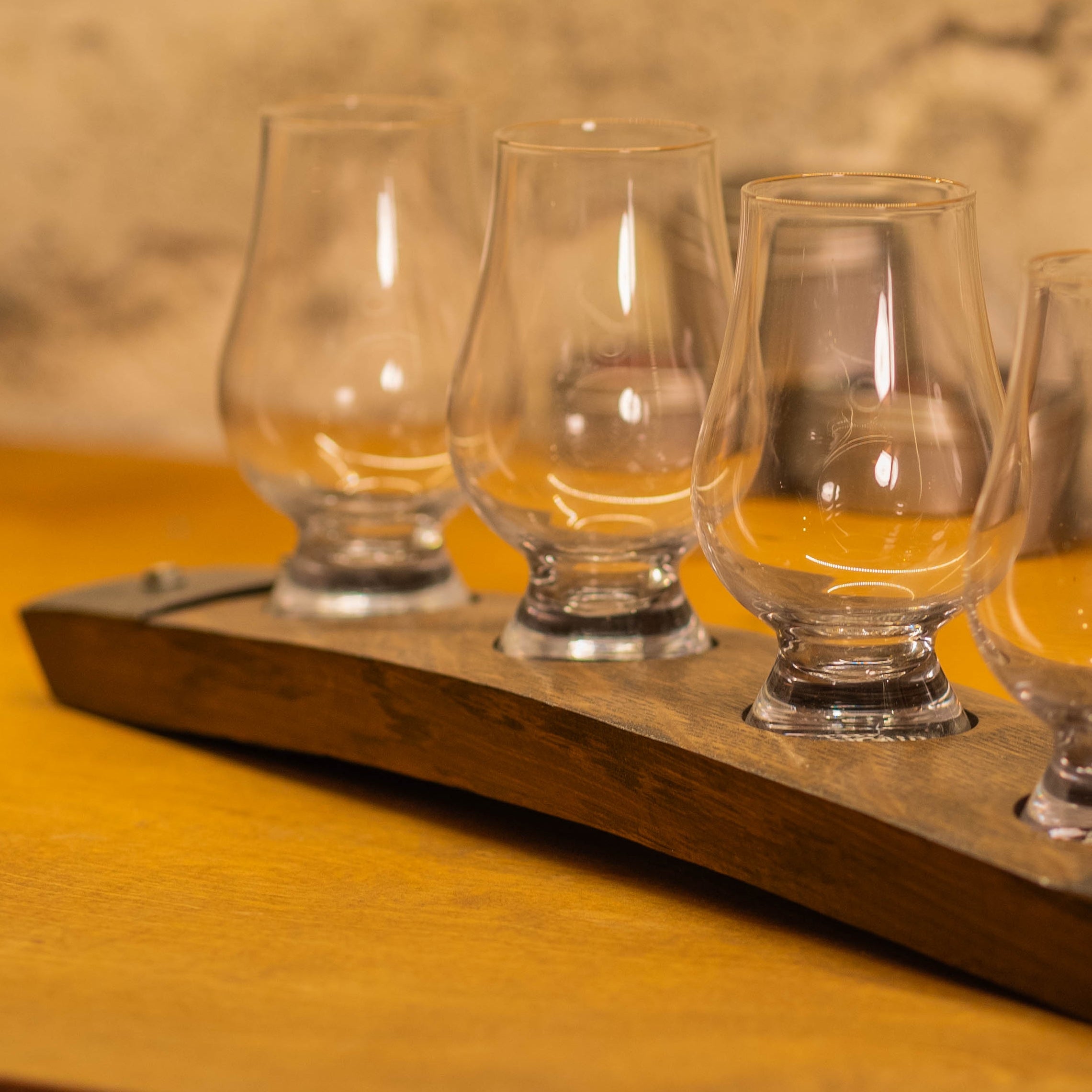 Close-up of Glencairn glasses seated in metal-mounted recesses on a curved reclaimed bourbon barrel stave tasting flight board.