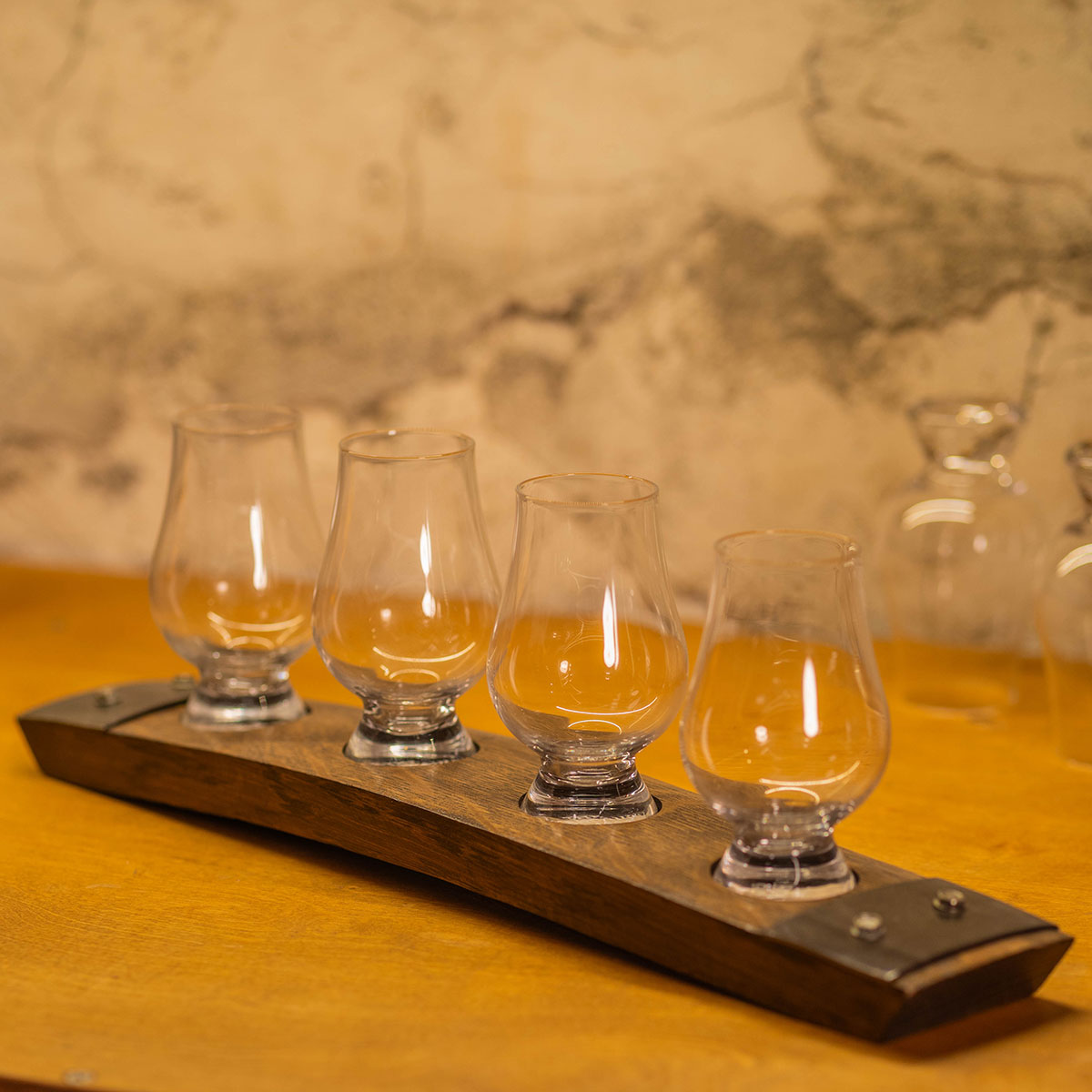 Four Glencairn glasses arranged on a reclaimed bourbon barrel stave whiskey flight board on a warm wood bar surface.