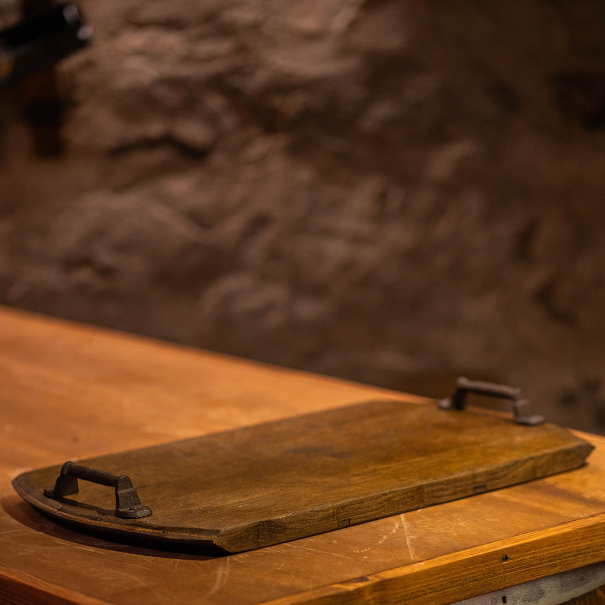 Reclaimed wood serving tray made from a wine barrel head resting on a wooden countertop, featuring dark metal handles and a rustic finish.