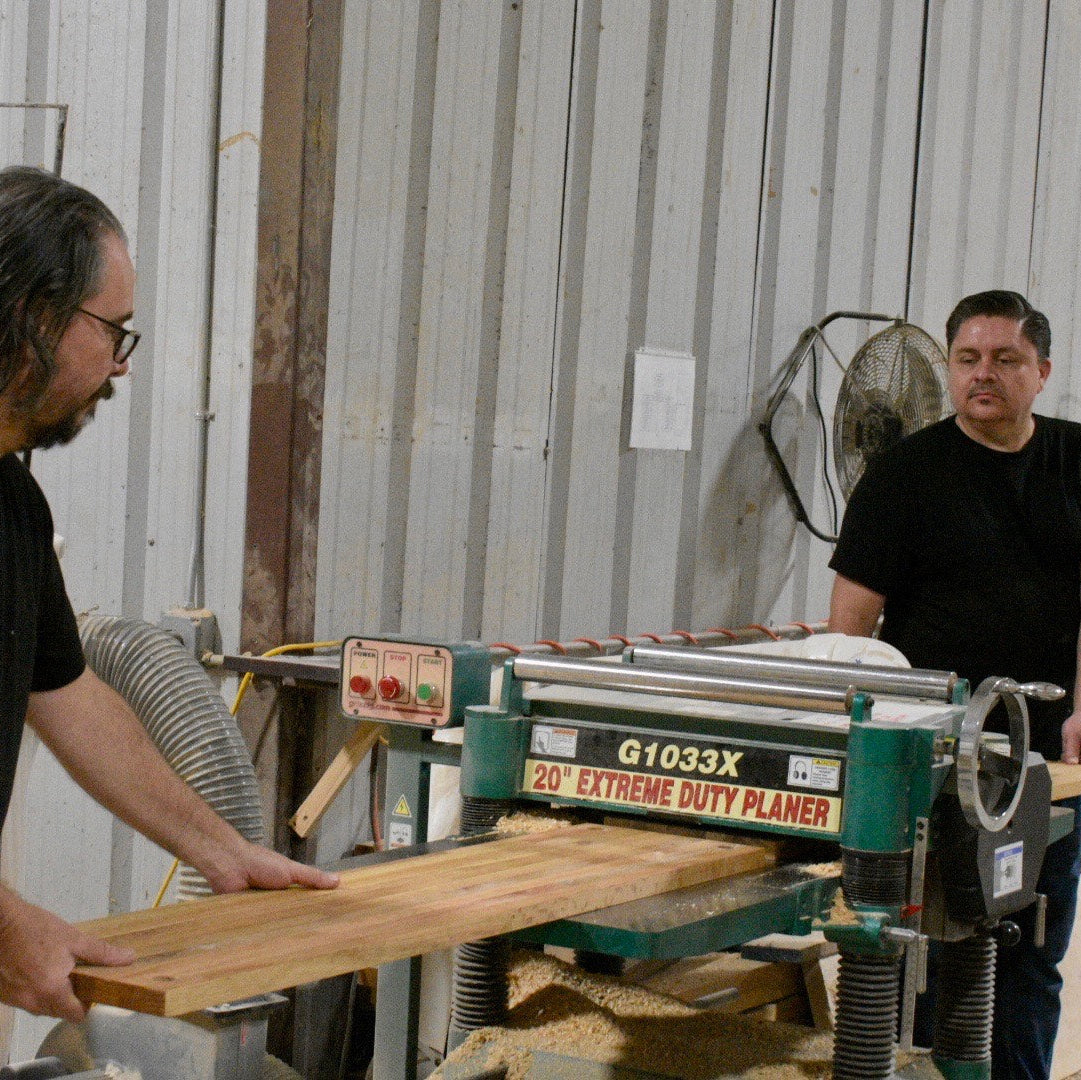 Two men working with a wood planer in a workshop.
