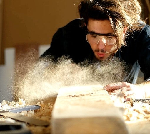 Artisan blowing sawdust from reclaimed wood project.