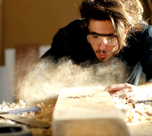 Artisan blowing sawdust from reclaimed wood project.