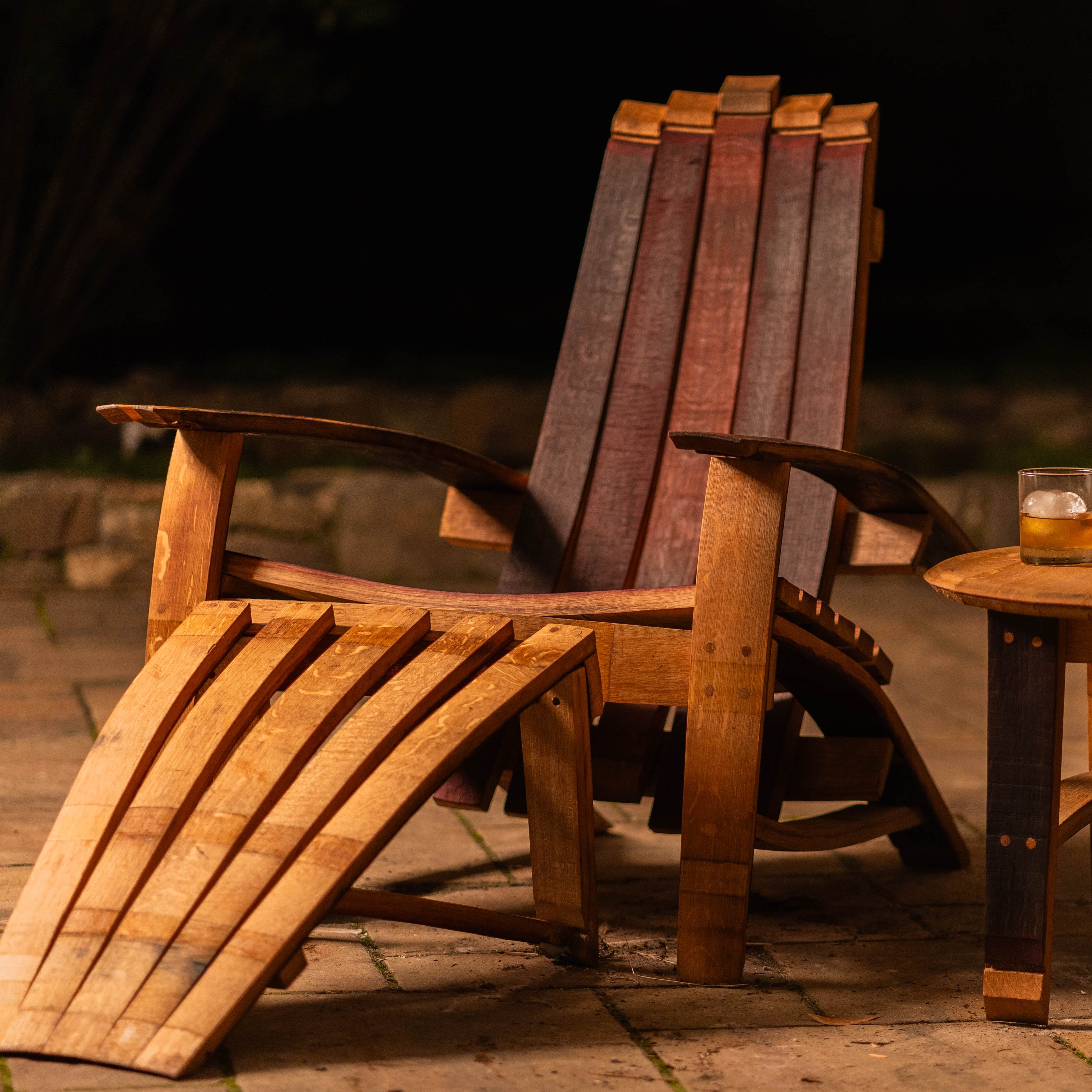 Cellr Wooden Adirondack Chair handcrafted from reclaimed wine barrel staves, shown outdoors with optional matching footstool in warm evening lighting.
