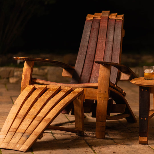 Cellr Wooden Adirondack Chair handcrafted from reclaimed wine barrel staves, shown outdoors with optional matching footstool in warm evening lighting.