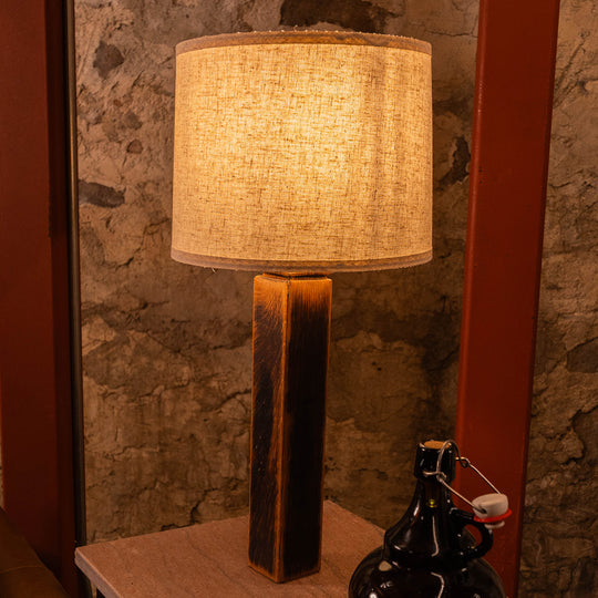 Charr Wooden Table Lamp with a fabric shade on a reclaimed barrel stave base, shown on a console table against a stone wall.