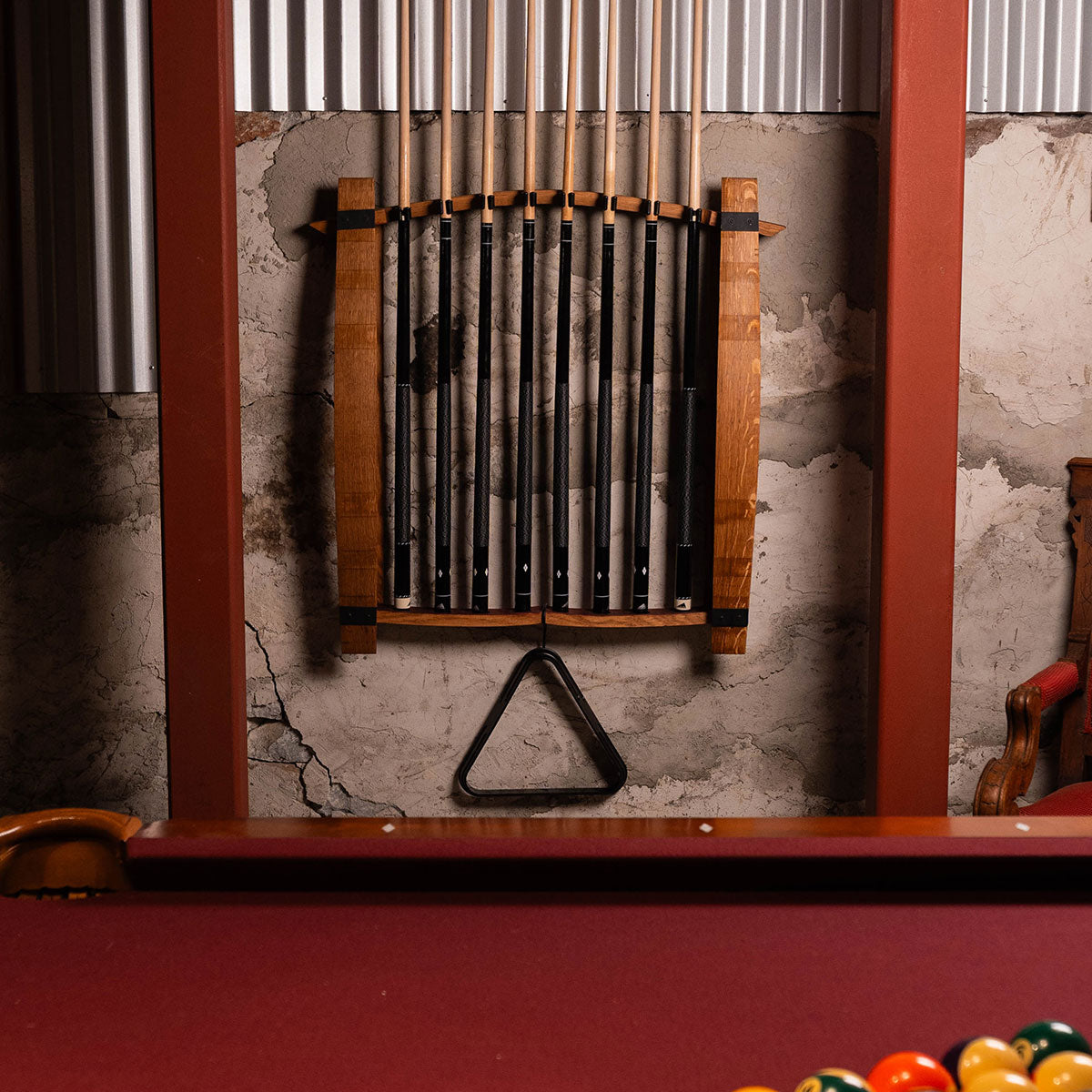 Pool cues in a rack on a textured wall with a pool table surface.