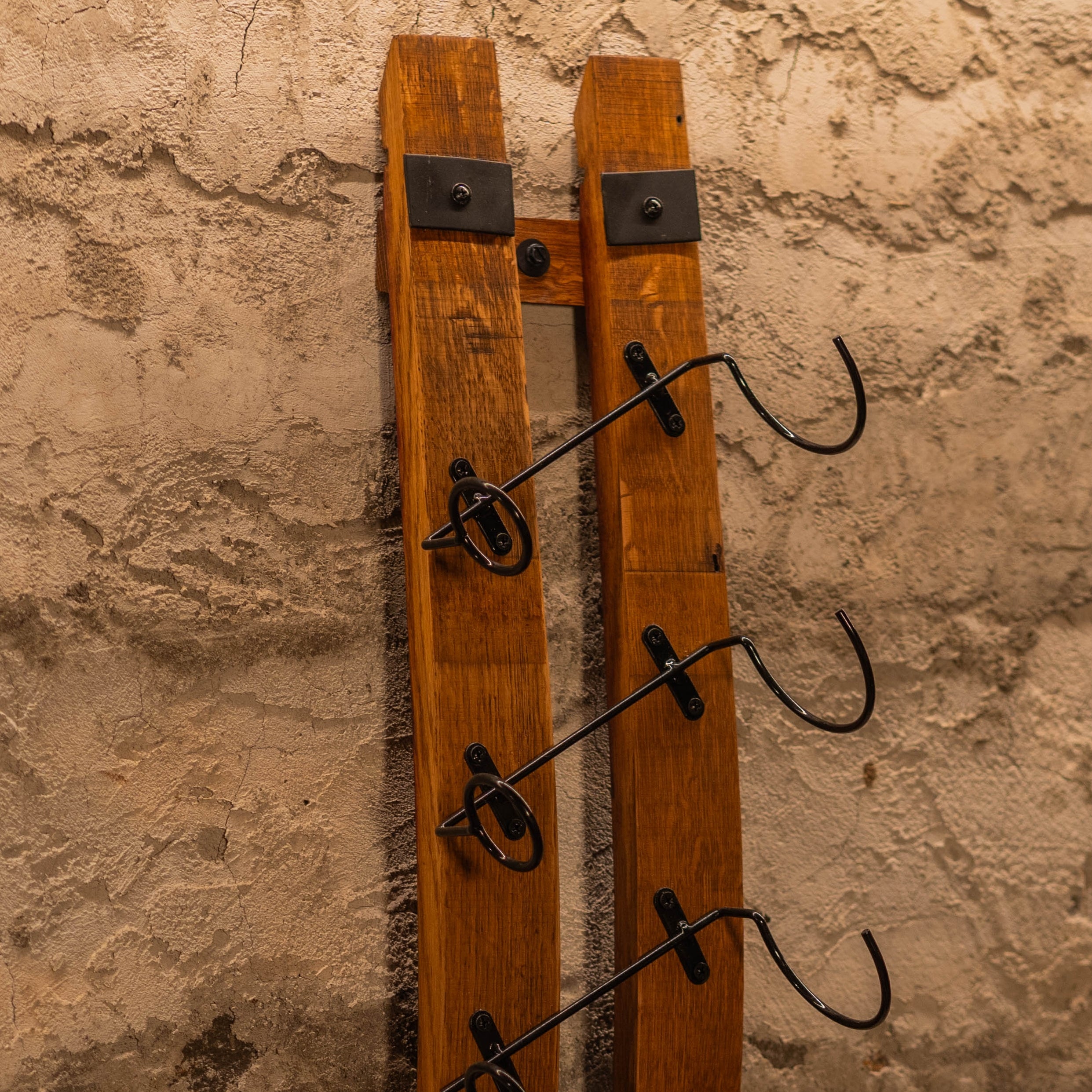 Barrel-stave wine rack shown empty, featuring steel wall brackets and curved metal bottle hooks.
