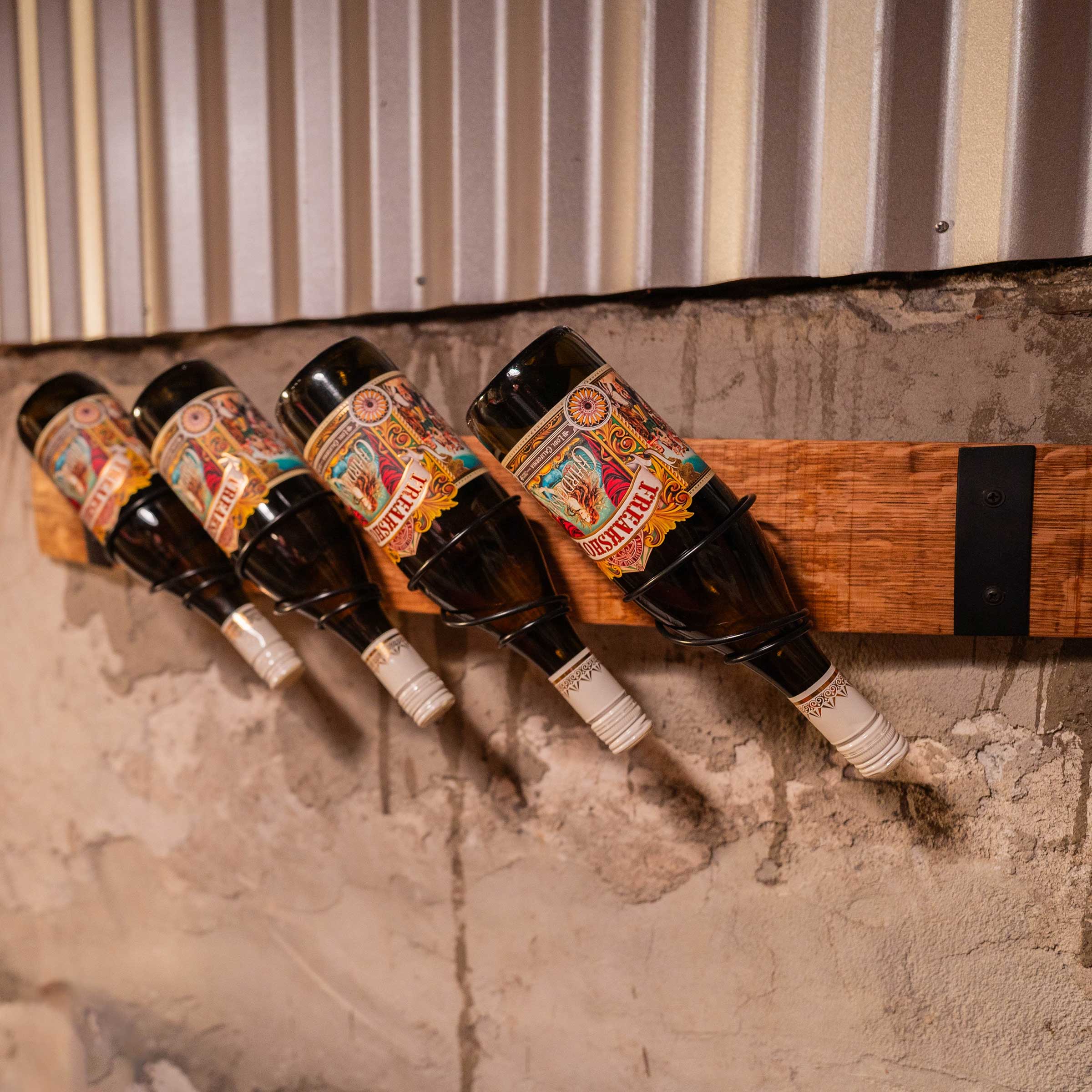 Four wine bottles displayed horizontally in a wall-mounted rack made from reclaimed barrel staves with black steel brackets.