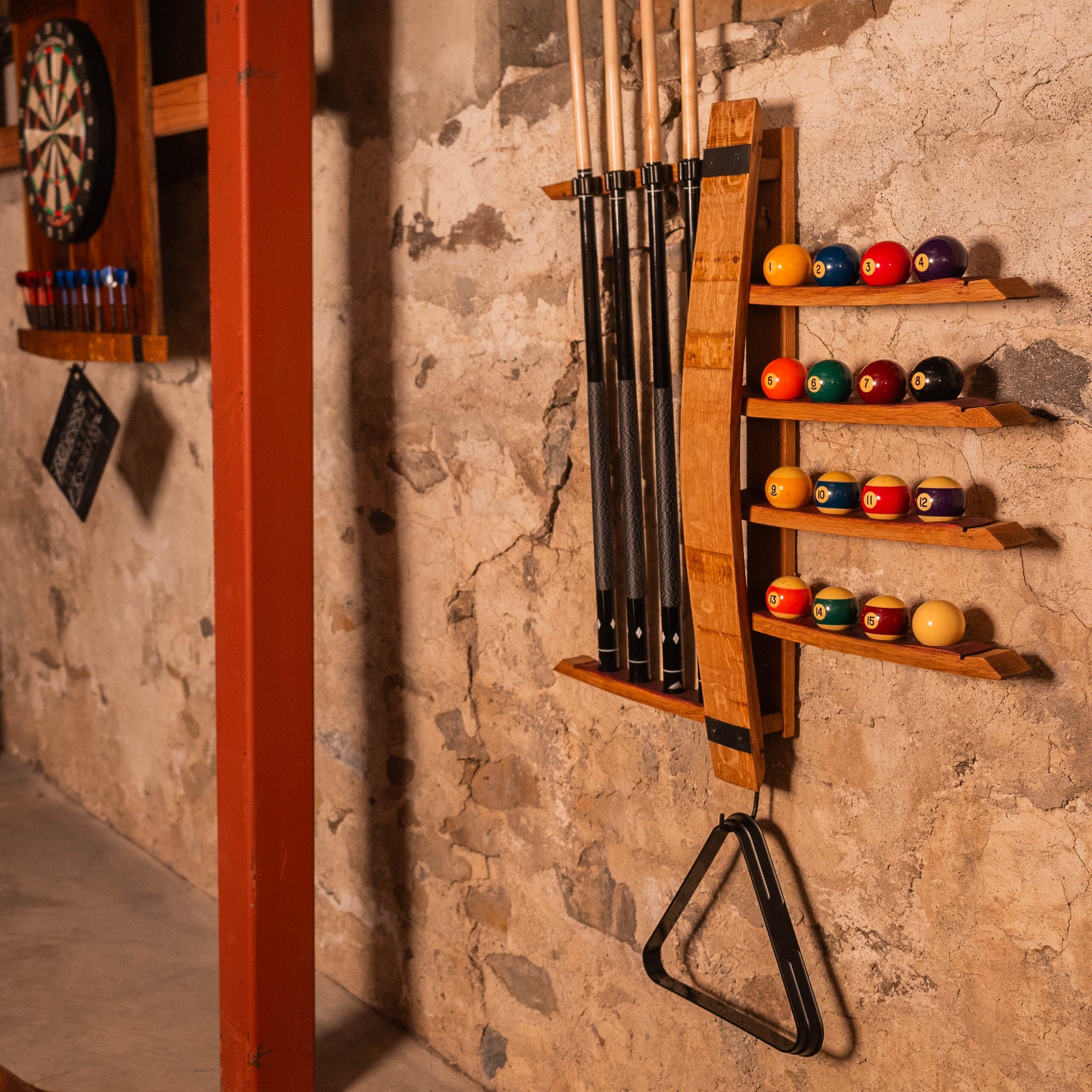 Wall-mounted pool cue rack with four cues and sixteen ball holder on rustic wall