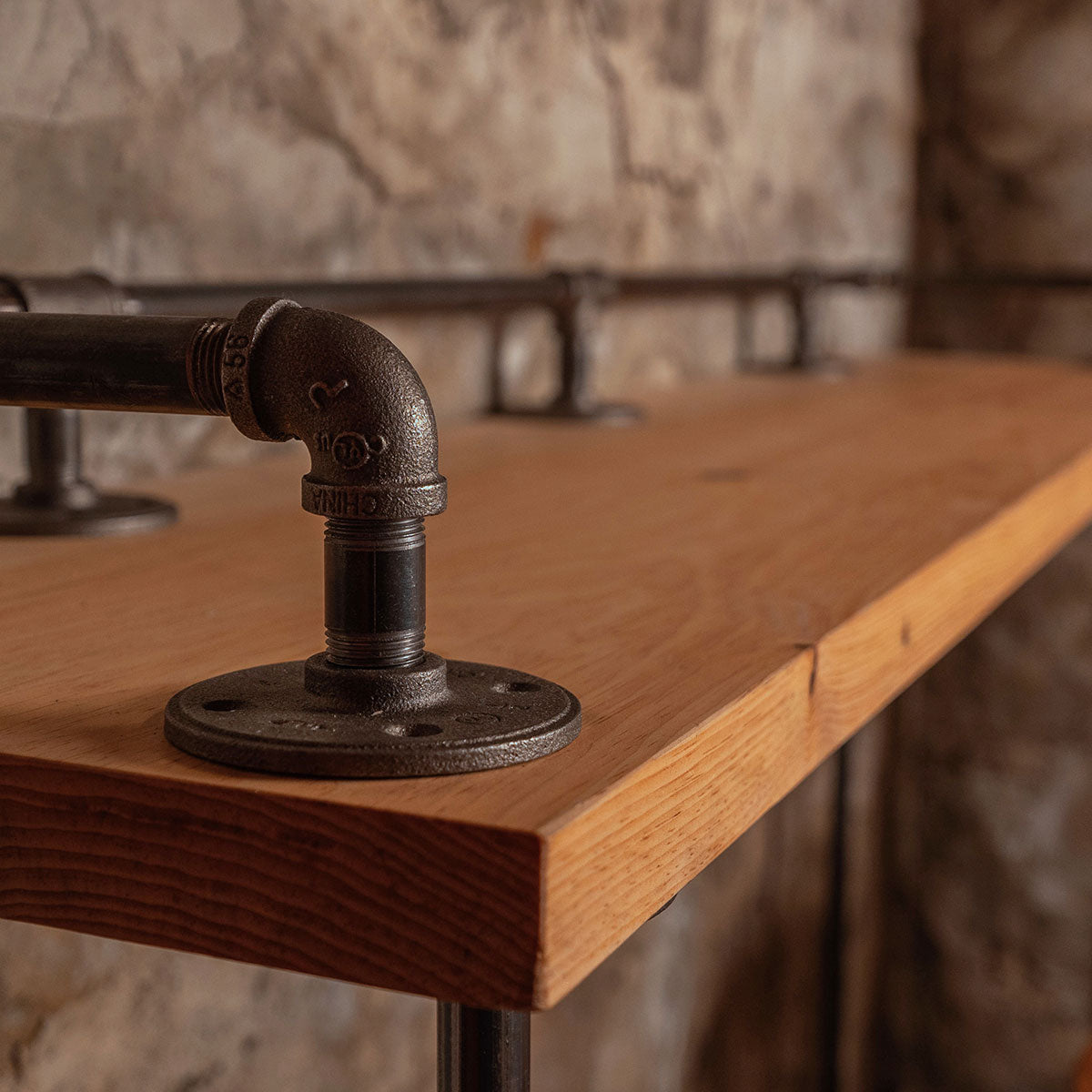 Wooden table with metal pipe support against a stone wall background