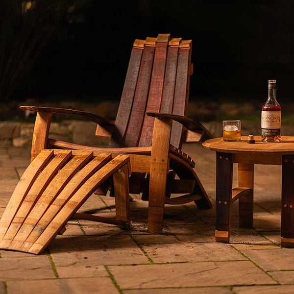 Wooden Adirondack chair with a bottle and glass on a small table outdoors.