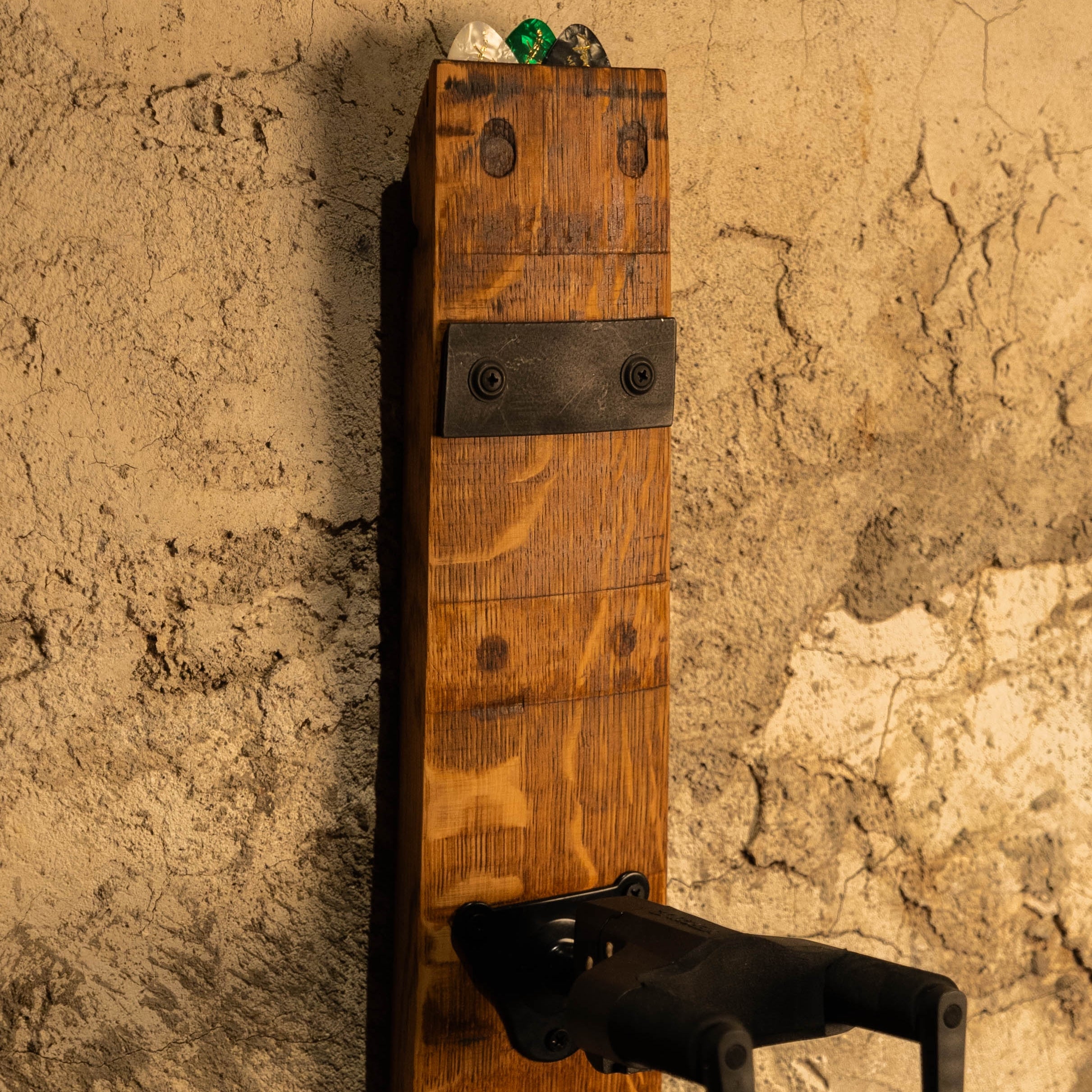 Side angle of a reclaimed barrel-stave guitar wall mount showing the locking yoke design.
