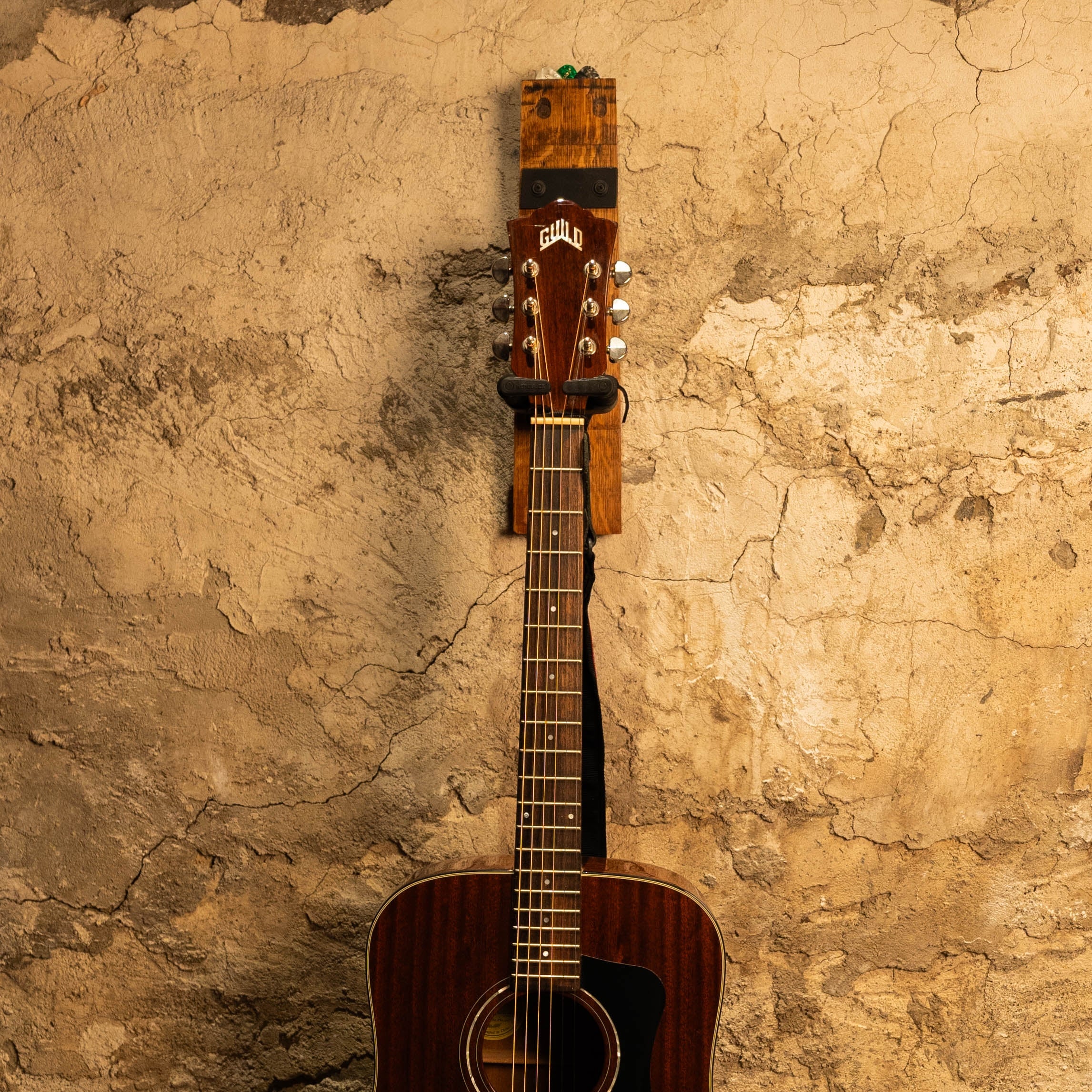 Acoustic guitar hanging on a reclaimed barrel-stave guitar wall mount with a locking yoke.