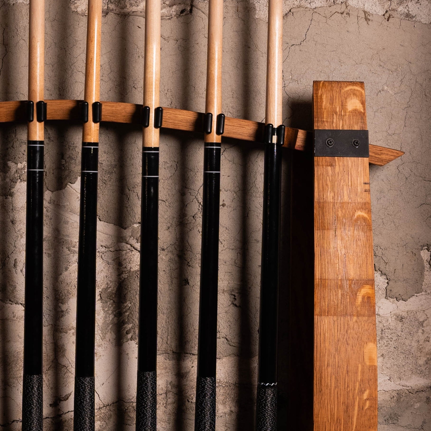 Close-up of pool cues snapped into quick-release clips on reclaimed barrel stave rack