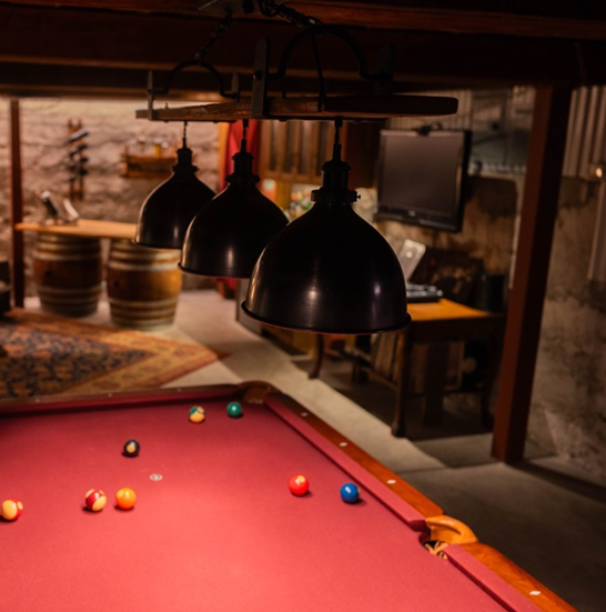 Pool table light fixture over a red velvet pool table in a home bar environment. Showing dimmed light for mood. 