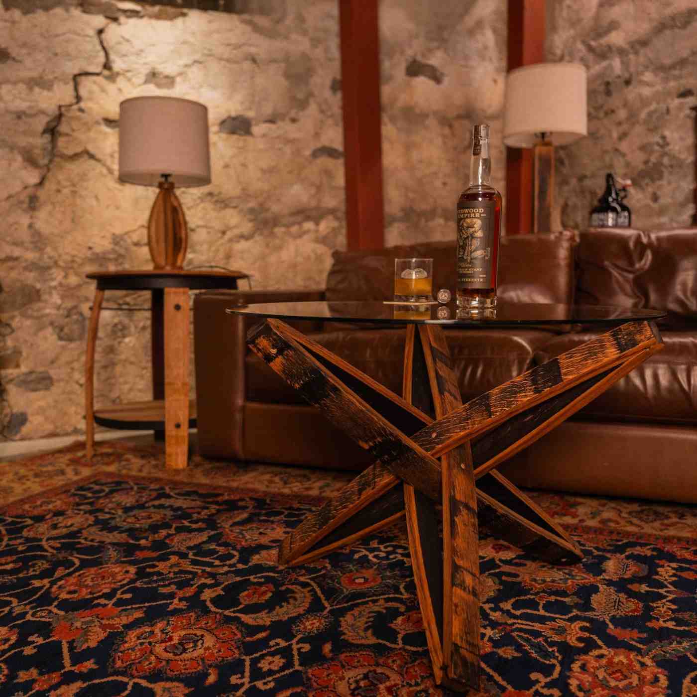 Stavv™ Whiskey Barrel Coffee Table in a lounge setting with whiskey glass and bottle, paired with reclaimed barrel furniture.