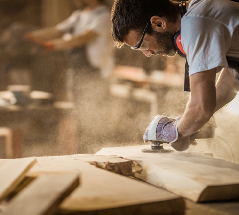 Man sanding a wooden surface with a sander in a workshop setting
