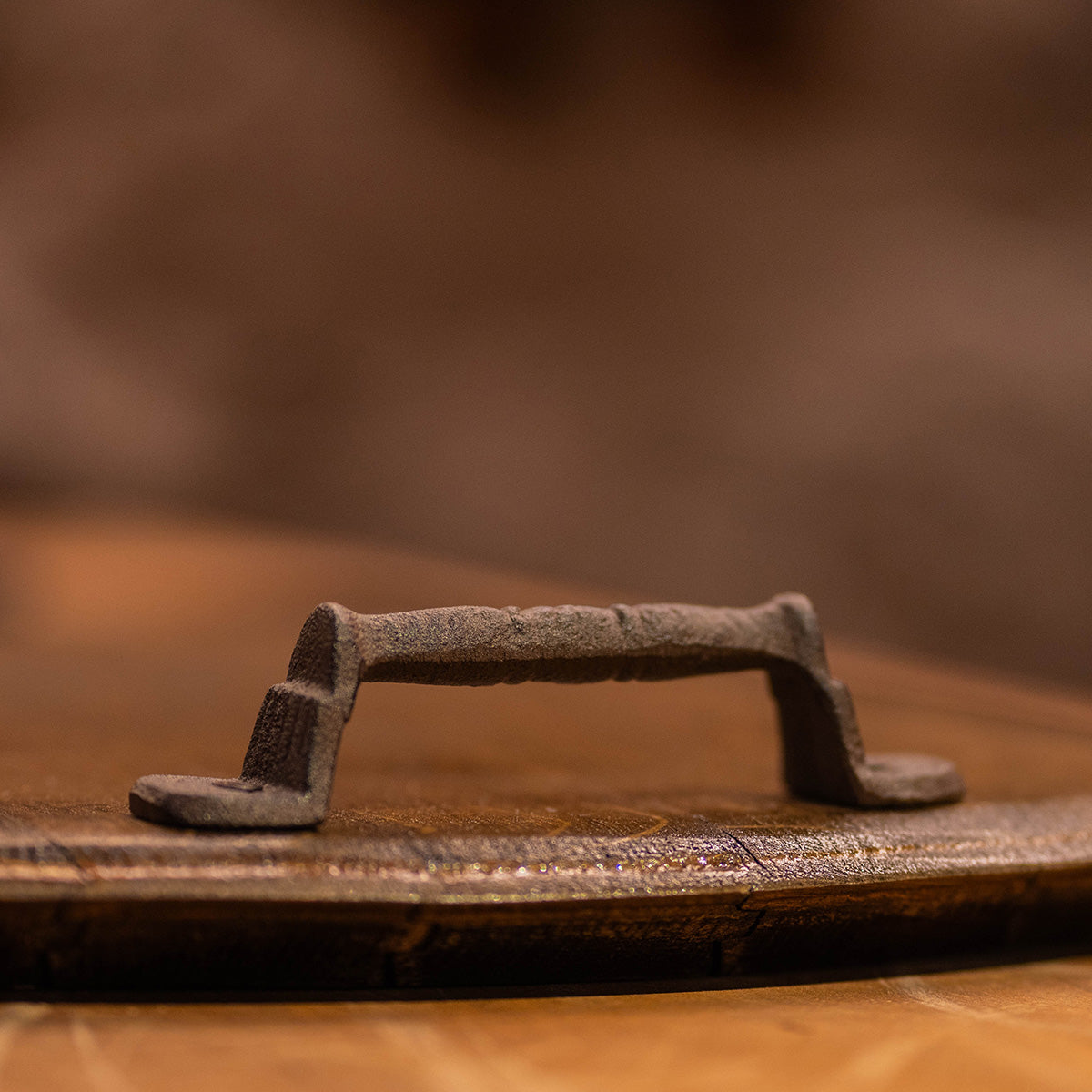 Close-up of the metal handle on a reclaimed wine barrel–head serving tray, showing the aged wood grain and textured iron hardware.